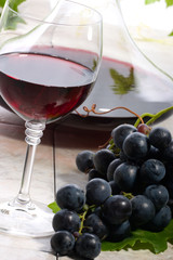 Glass of red wine, decanter and fresh cut black wine grape
