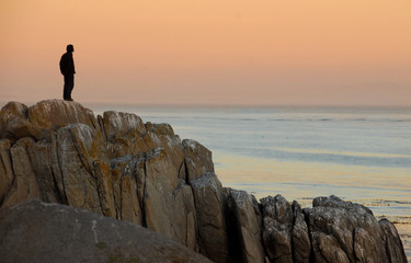 Man by himself on cliff overlooking sea - 10166972