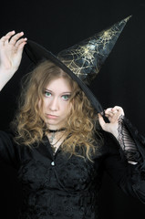 Cute young witch in hat, on black background