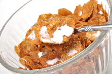 Tilted view of wheat bran flakes cereal in spoon and bowl.