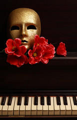 gold mask and red flower on a piano
