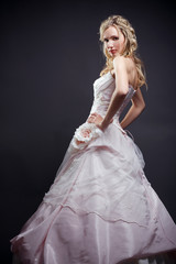 Fototapeta na wymiar Beautiful blond bride wearing wedding dress posing on gray