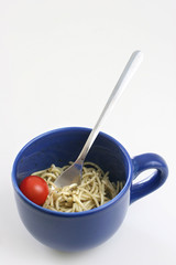 Pasta olio with a cherry tomato in a large blue ceramic cup