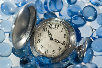Antique watch under water on blue glass pebbles