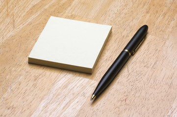 Pen and Post It Notes Pad Against a Wood Background