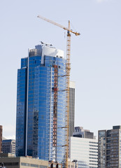 Fototapeta na wymiar A yellow construction crane erecting a high rise blue glass
