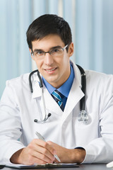 Happy doctor with stethoscope writing at office