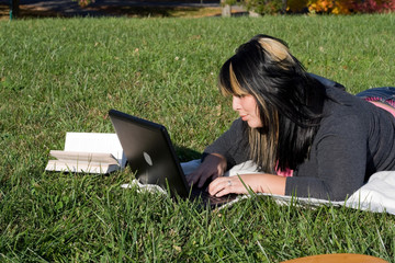 A young student using her laptop computer laying in the grass