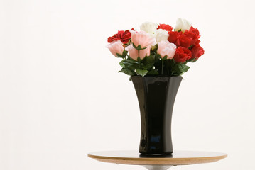 Red,and pink roses in a black vase on table over white