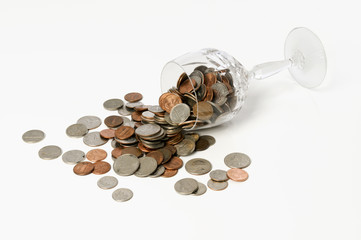 Crystal goblet filled with coins spilling on table over white