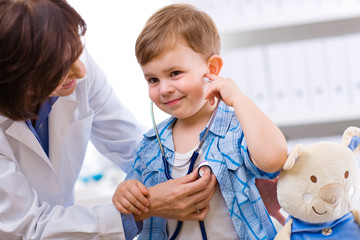 Senior female doctor examining happy child, smiling.
