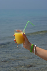 Glass of juice in human hand with sea on background