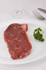 raw steak on a white plate with cutlery