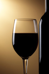 A glass of red wine and bottle, brown graduated background.