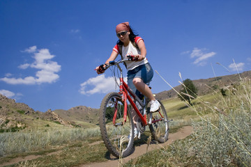 Girl rides a bike in mountains.