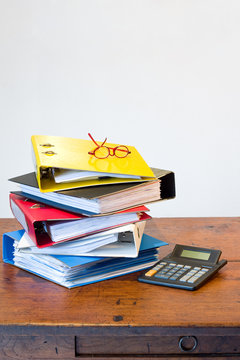 Colored ring binders, glasses & calculator on wooden desk