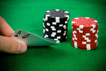 Two aces in male hand with black and red poker chips.