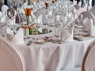 Bankett-Esstische mit rosa und weißer Tischdecke, Weingläsern, Stoffservietten, Besteck und roten Rosen auf einem Spiegelmittelstück
