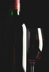 Glass and bottle of red wine on black