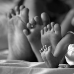 cute newborn foot with siblings feet behind her