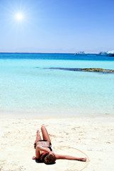 Young girl in bikini lying on white sand beach