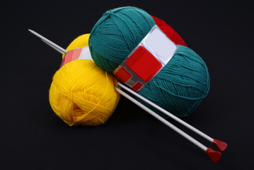 three woolen skeins and knitting needle.. on black background