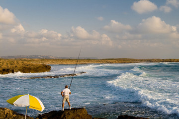 Fisherman on the beach with white and yellow sunshade