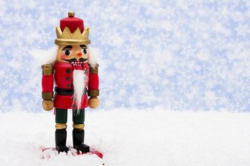 Nutcracker sitting on snow with snowflake background