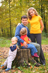 Fototapeta premium Parents with children sit on stub in forest in autumn.