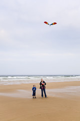 Obraz premium Mother and son plus baby daughter looking up at kite on beach