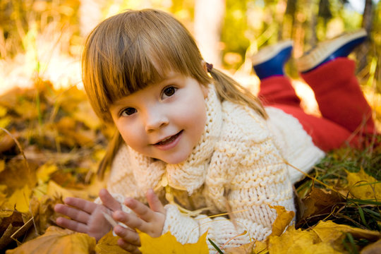 Small adorable girl lying on golden leaved ground
