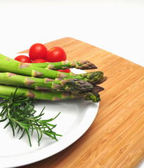 Asparagus spears on a white plate with cherry tomatos