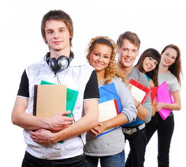 Group of  young  joyful students standing with book and bags.