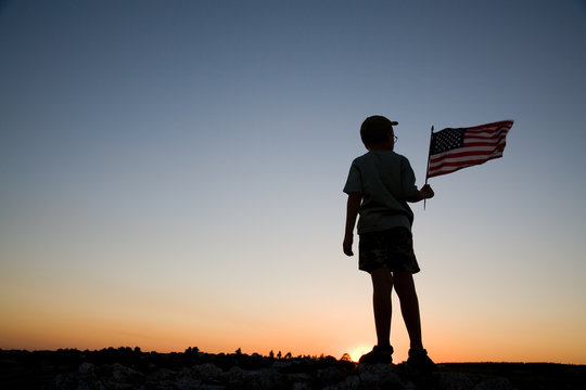 Young boy holding an American flag at sunset.