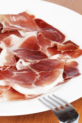 Slices of tasty spanish ham on white dish. Shallow DOF