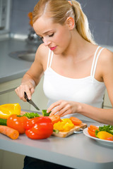 Obraz na płótnie Canvas Young woman making salad at kitchen