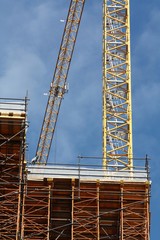 Détail de deux grues sur un chantier de construction avec vue sur le bâtiment en cours de construction et les échafaudages