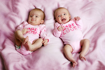 fraternal twins on a pink blanket are smiling