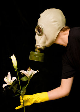 person in a gas mask smells a flower