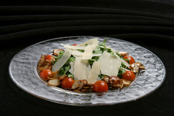 Salad from rukkola with parmesan, tomatoes and mushrooms.