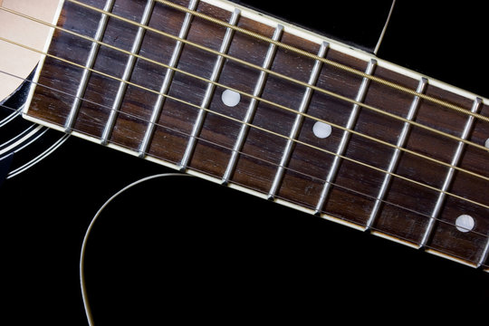 Close-up of fingerboard and strings on black acoustic guitar