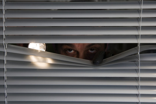 Einbrecher mit einer Taschenlampe sieht durch ein Fenster