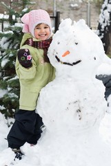 Cute little girl playing in winter backyard with a huge snowman