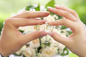 Bride and groom holding two rings over wedding bouquet