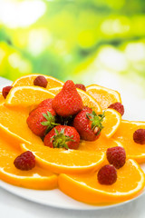 Plate with orange, strawberry and raspberry, outdoors