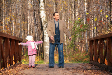 Grandfather with  granddaughter  on wooden bridge  in autumn