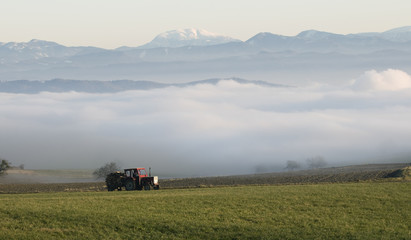 Traktor am Feld mit Herbstnebel und Alpen