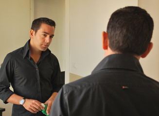 uomo con camicia scura ed orologio si guarda allo specchio