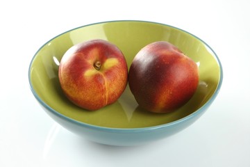 Two red peaches in a green dish
