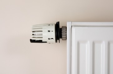 White radiator with thermostat on beige (wall) background